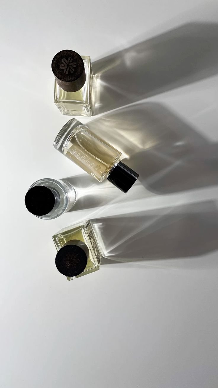 Alt Text: A minimalistic arrangement of four elegant perfume bottles casting soft shadows on a white background, symbolizing the journey to discovering a signature scent.