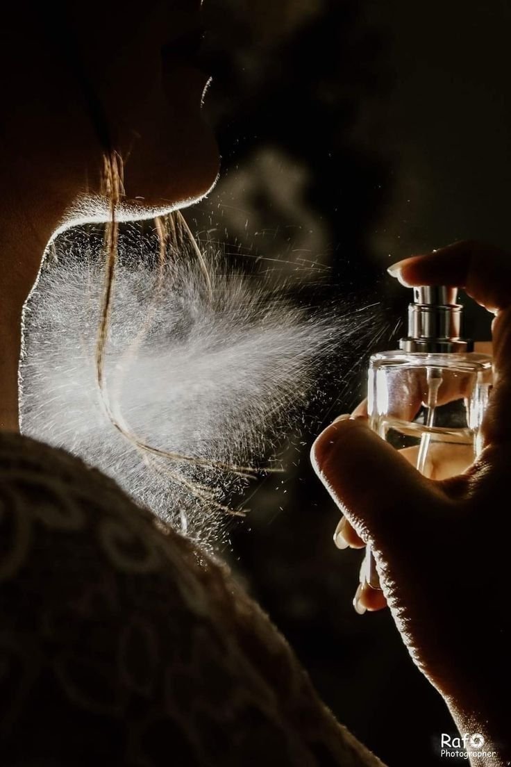 A close-up of a person spraying perfume on their neck, with the mist visibly dispersing in the air, illustrating how perfume interacts with skin.