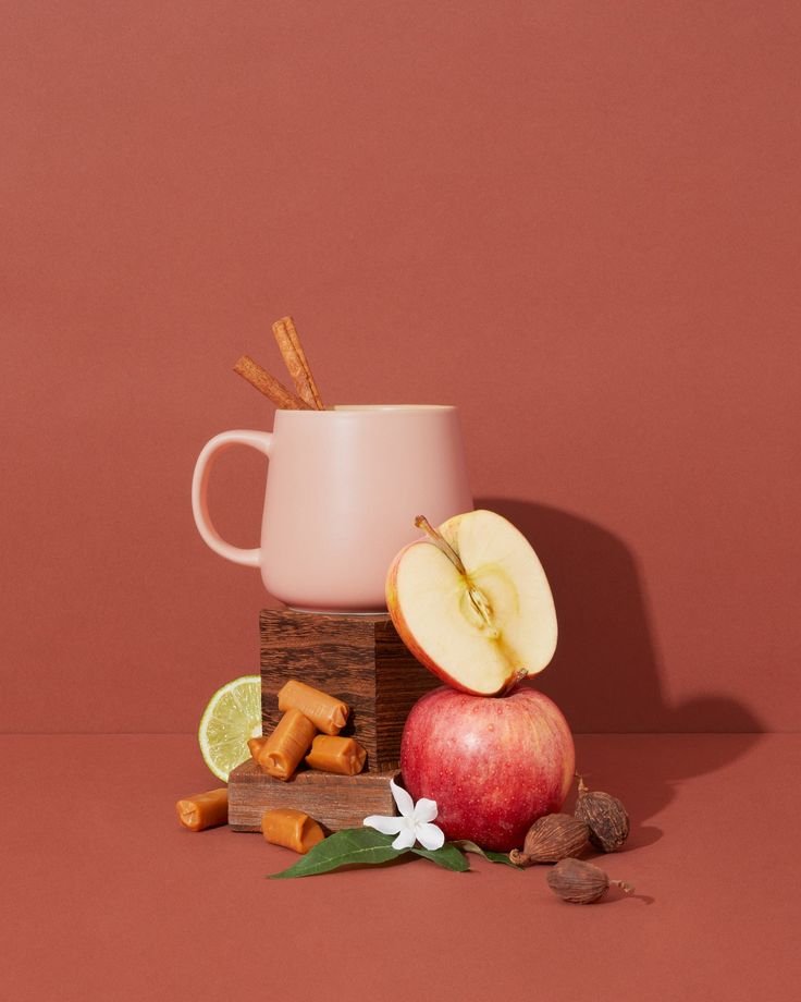 A curated arrangement featuring an apple, cinnamon sticks, caramel, and other natural elements on a warm background, symbolizing fragrance families.