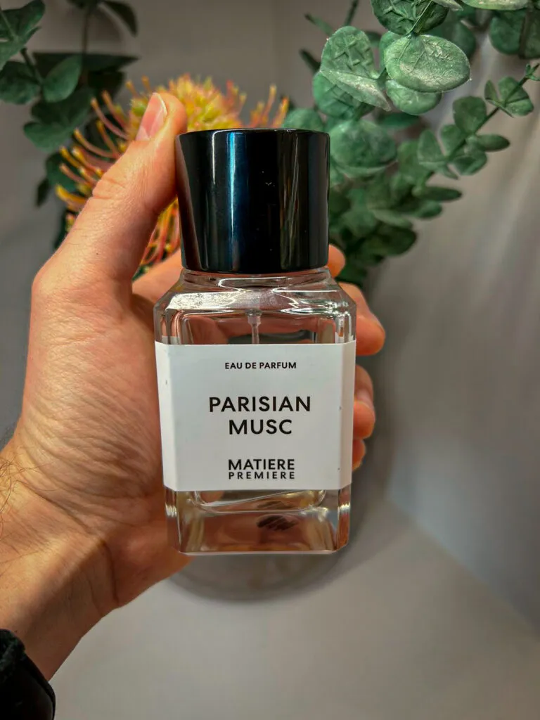 Bottle Of Matiere Premiere Parisian Musc being held by ha young man's hand with a plant in the background