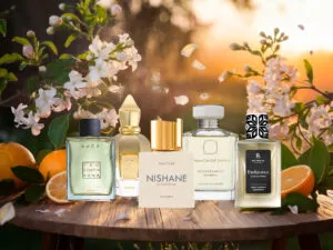 A collection of five niche spring perfumes displayed on a rustic wooden table, surrounded by blooming white flowers, fresh citrus fruits, and a golden sunset in the background. spring niche perfumes, best spring fragrances for men, luxury perfumes for spring, fresh and citrusy perfumes, top men’s niche scents, long-lasting spring perfumes, floral and woody fragrances, elegant niche colognes
