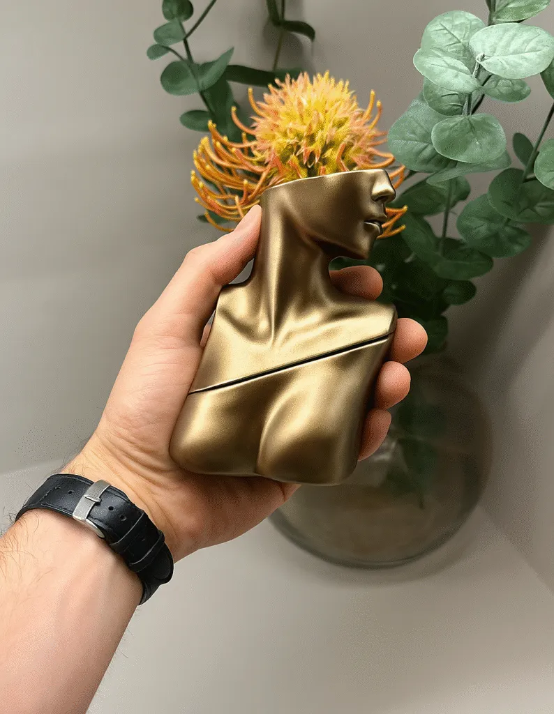 Hand holding the Billie Eilish Eau de Parfum bottle shaped like a metallic bronze bust, featured in the Billie Eilish Fragrance Buying Guide.