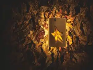 Mugler Pure Havane perfume bottle glowing with amber light, surrounded by tobacco leaves, symbolizing its warm honeyed tobacco fragrance character.