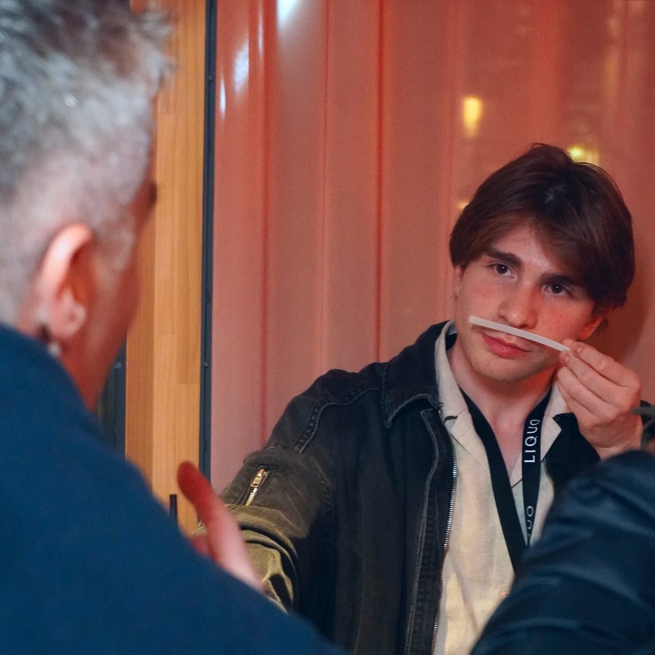 Smelling a fragrance test strip while engaged in conversation at a LIQUO event, fully absorbed in the world of niche perfumery.